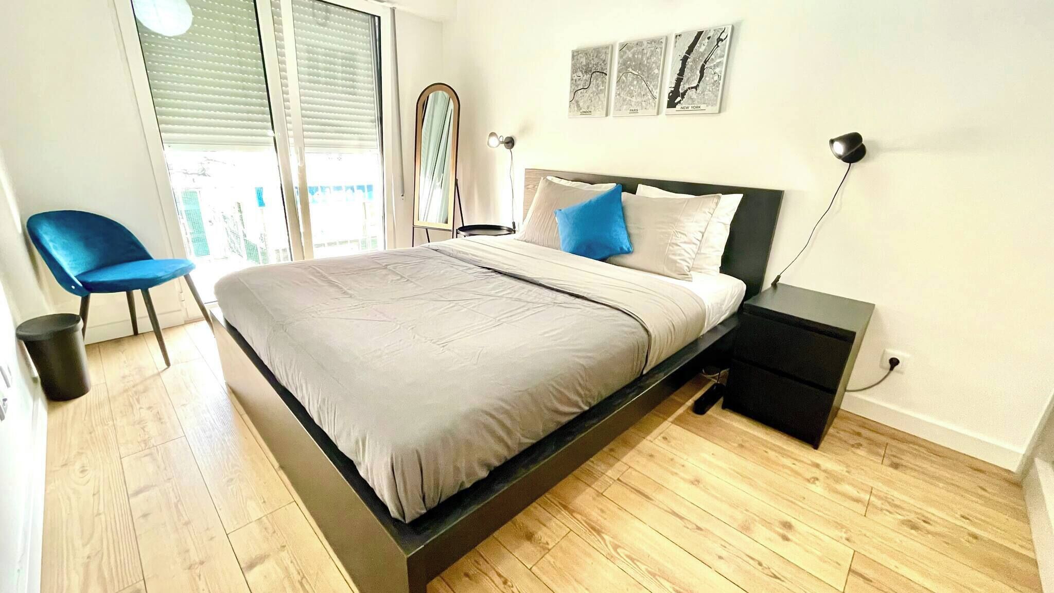 Een moderne slaapkamer met een bed, nachtkastjes, een stoel en een raam met zonwering.