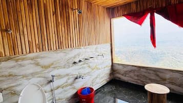 A bathroom with a wooden ceiling, marble walls, a toilet, a red bucket, and a view through a window.