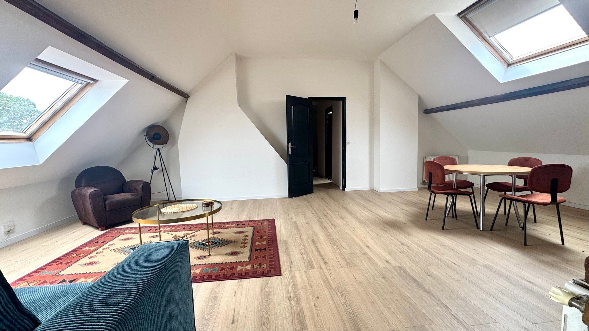 Un appartement-loft spacieux avec de hauts plafonds, des fenêtres de toit, un coin repas avec des chaises rouges, un canapé et un lampadaire.