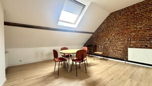 A loft-style room with a brick wall, a skylight, a round table with chairs, and a radiator.