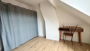 A room with a wooden desk and chair, a grey curtain, and a sloped ceiling.