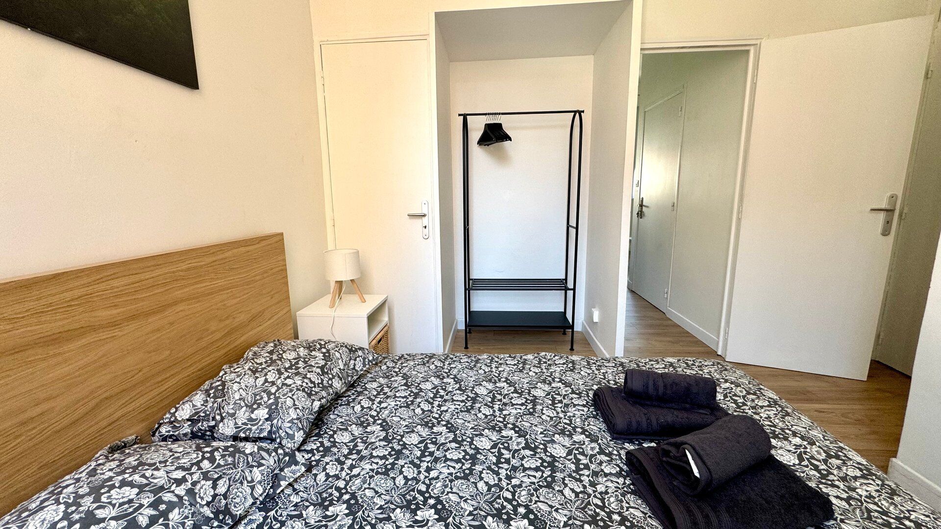 Een slaapkamer met een bed, een nachtkastje, een lamp, een kledingkast en een deur naar een andere kamer.