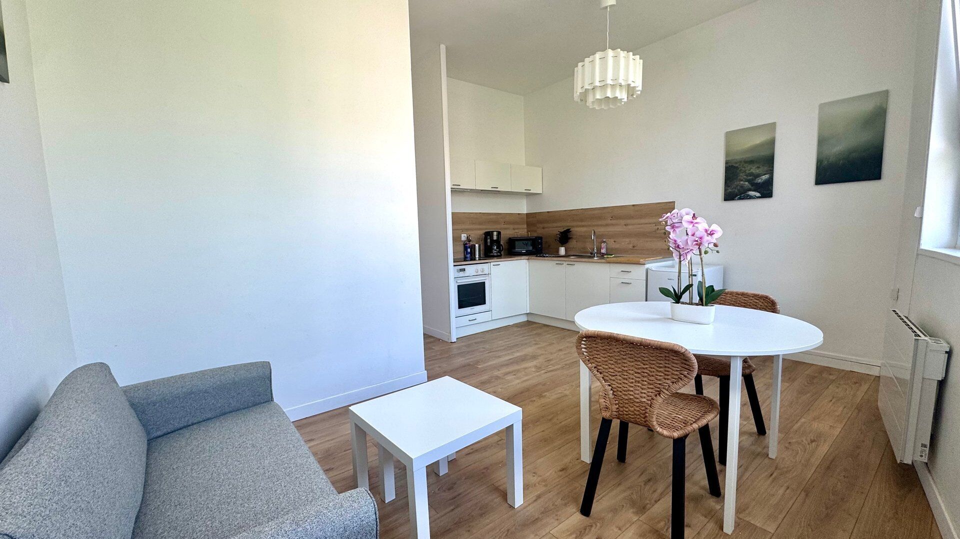 Une cuisine moderne avec des meubles blancs, une table à manger entourée de chaises en osier et une petite table blanche.
