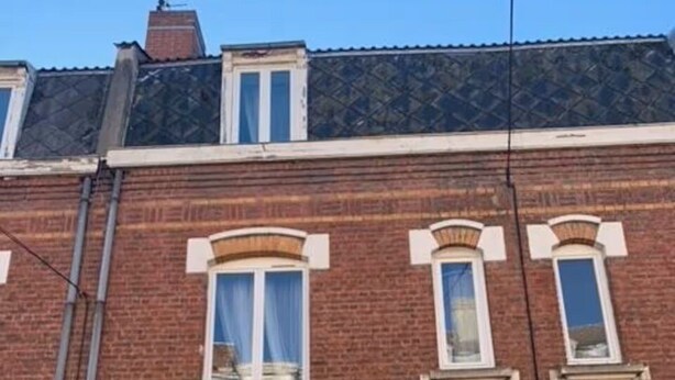 Un bâtiment en briques de deux étages, avec une porte noire et des fenêtres à cadre blanc.