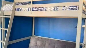 Un lit superposé avec une assise rembourrée grise, une petite table et des murs bleus.