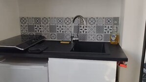 Une cuisine de taille réduite avec un plan de travail noir, un réfrigérateur blanc et un crédence décorée.