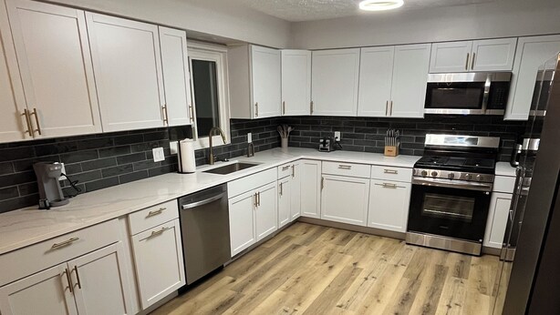 A modern kitchen with white cabinets, a black backsplash, and a wooden floor. - Luxury Entertainers Escape—Game Room + Lounge (Davenport)
