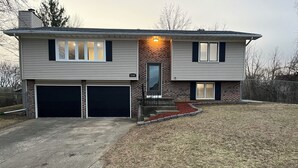 A two-story house with a garage, a brick section, and a well-maintained lawn. - Luxury Entertainers Escape—Game Room + Lounge (Davenport)