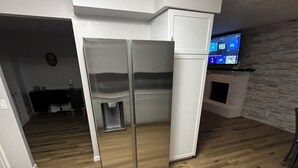 A kitchen with a stainless steel refrigerator, wooden flooring, a built-in oven, and a television mounted on the wall. - Luxury Entertainers Escape—Game Room + Lounge (Davenport)