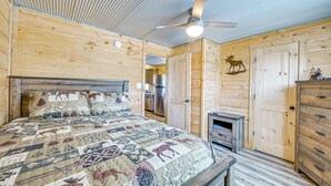 A wooden cabin interior with a bed, a ceiling fan, a fireplace, and a wooden wardrobe. - Fire Pit, Grill! Mammoth Cave Cabin Near Boat Ramp (Mammoth Cave)