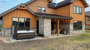 A modern two-story house with a stone exterior, a covered patio with outdoor seating, and a hot tub. - Granby Mtn Retreat w/ Ski Hill Views, Hot Tub (Granby)