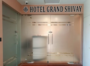 A hotel entrance with a frosted glass door and a sign reading 'HOTEL GRAND SHIVAY'.