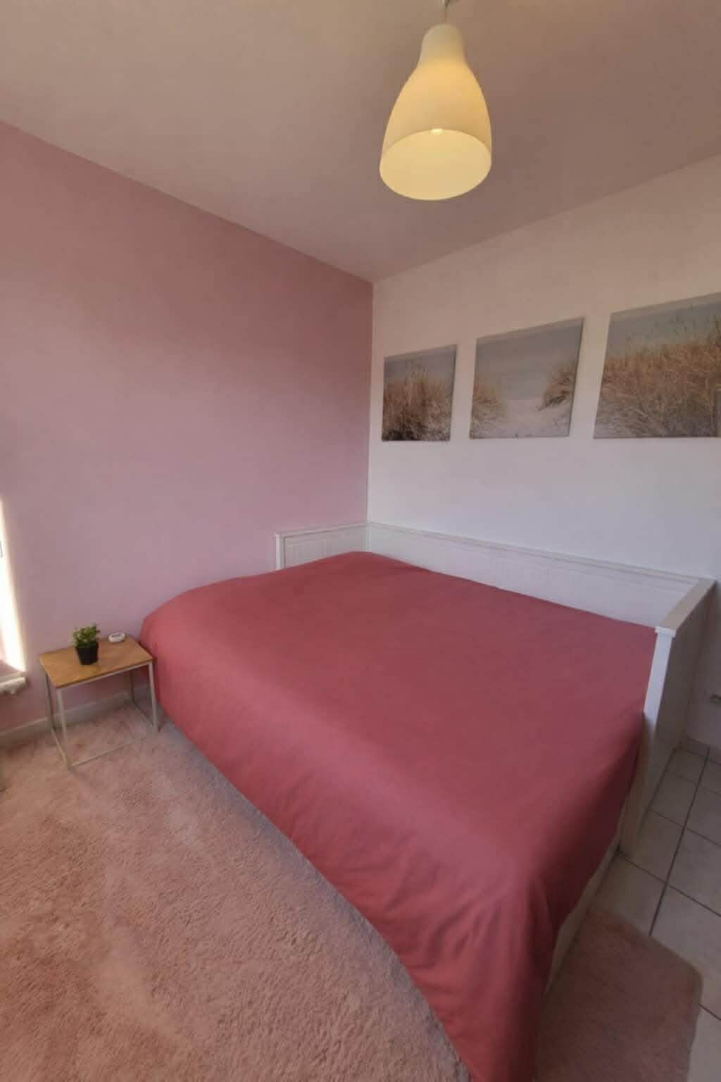 Une chambre à coucher avec un lit, une table de chevet ornée d’une plante et un mur sur lequel sont accrochés trois tableaux.