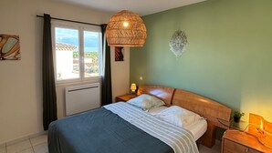 A bedroom with a bed, a bedside table, a lamp, a wall decoration, and a window with curtains.