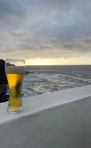 Ein Bierglas auf einem Vorsprung mit Blick auf den Ozean und einen bewölkten Himmel.