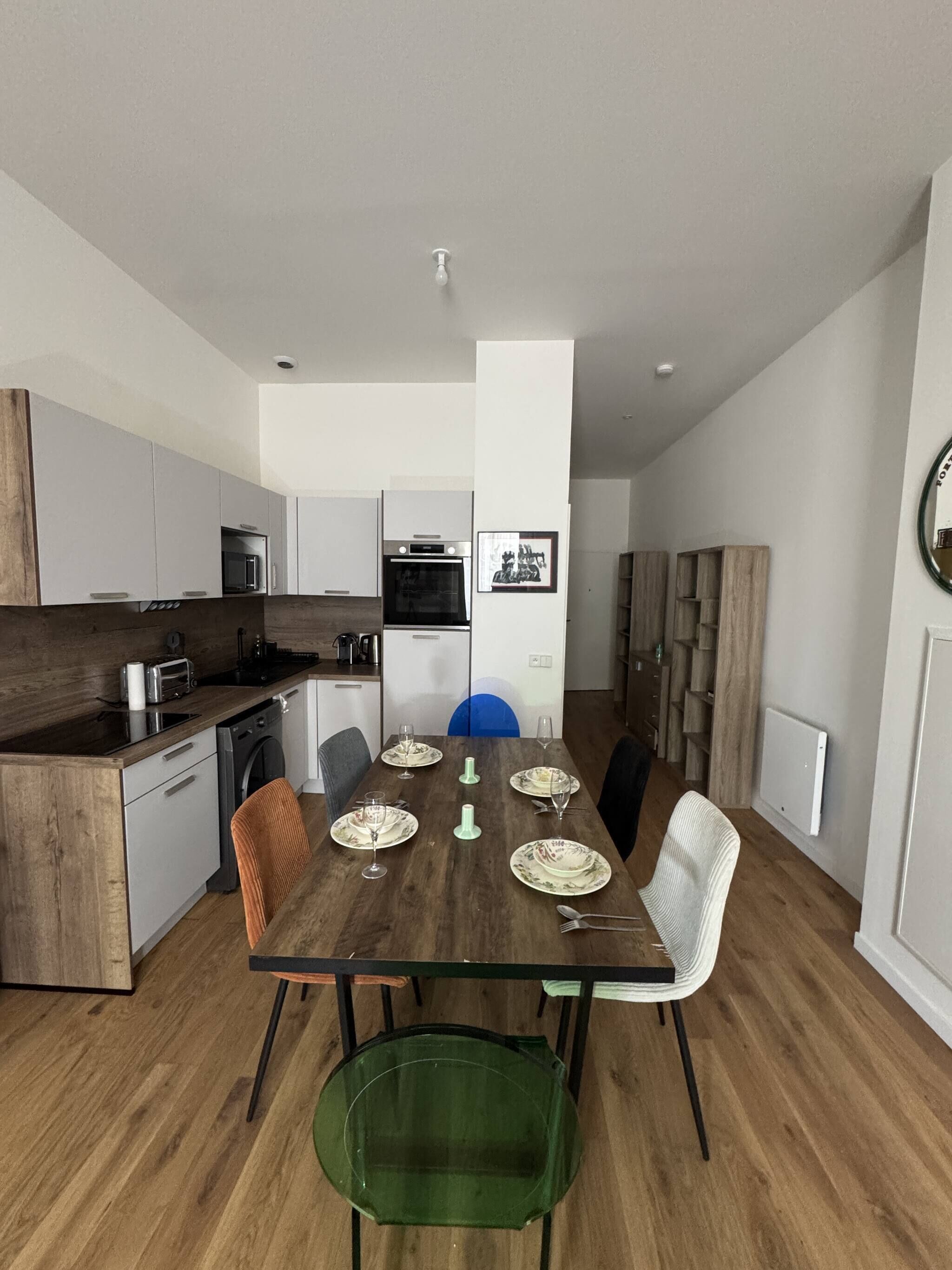 Une cuisine moderne avec un coin repas, comprenant une table en bois dressée pour six personnes, un lave-vaisselle et un four à micro-ondes.