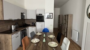 A modern kitchen with a dining area, including a wooden table set for six, a dishwasher, and a microwave. - Elegant 2-Bedroom Apartment in the Heart of Paris (Paris)