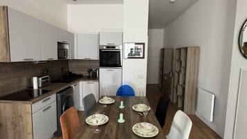 Une cuisine moderne avec un coin repas, comprenant une table en bois dressée pour six personnes, un lave-vaisselle et un four à micro-ondes.