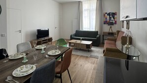 A modern living room with a dining area, a sofa, a TV, and a lamp. - Elegant 2-Bedroom Apartment in the Heart of Paris (Paris)