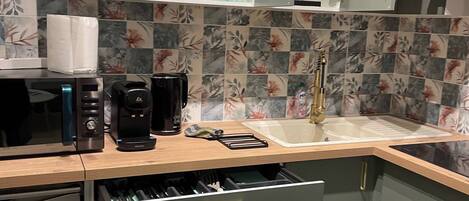 A modern kitchen with a microwave, coffee maker, and a sink. There are cabinets and a countertop with various items.