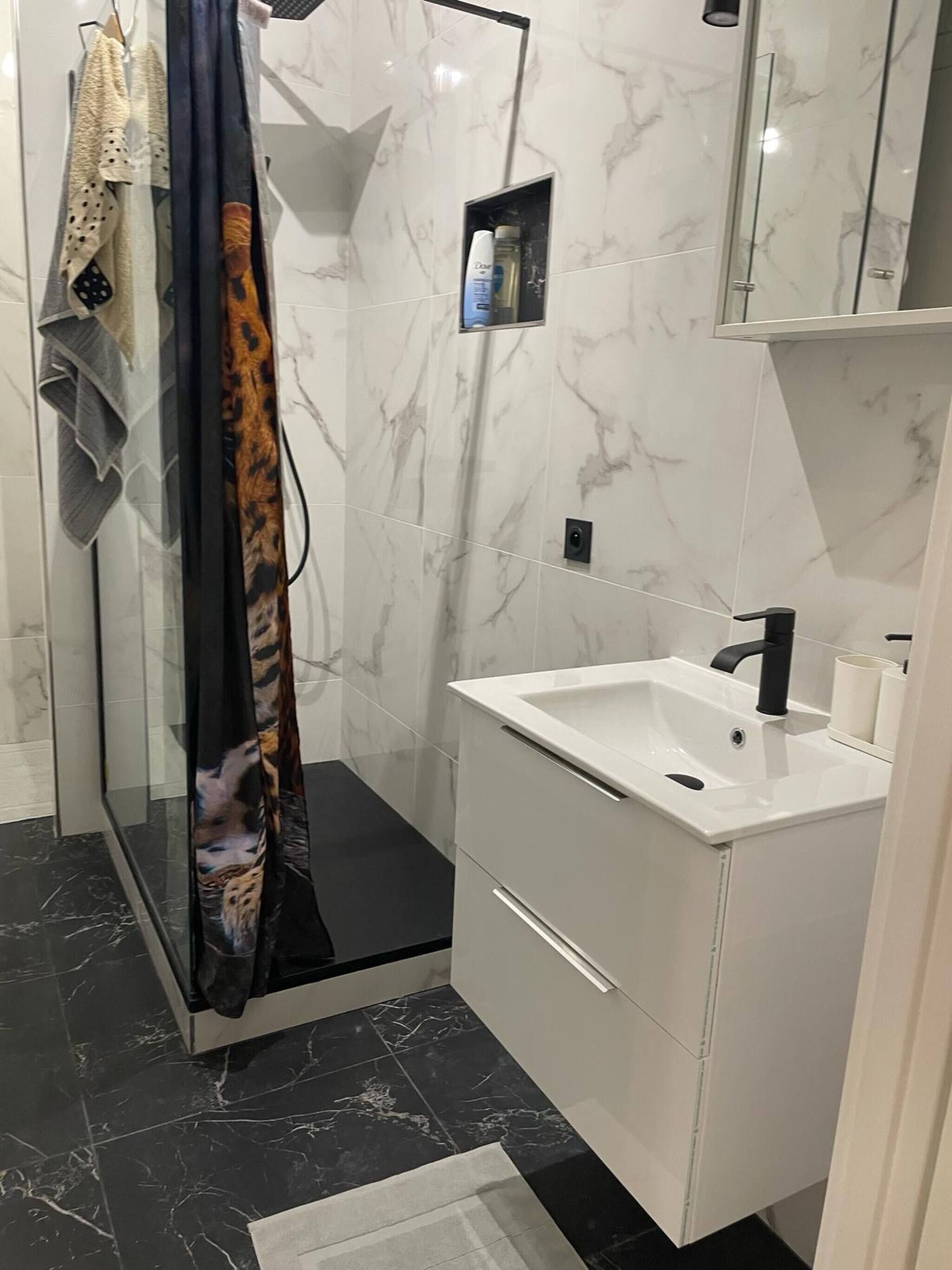 Un baño con cabina de ducha de vidrio, un lavamanos blanco y suelo de baldosas de mármol.