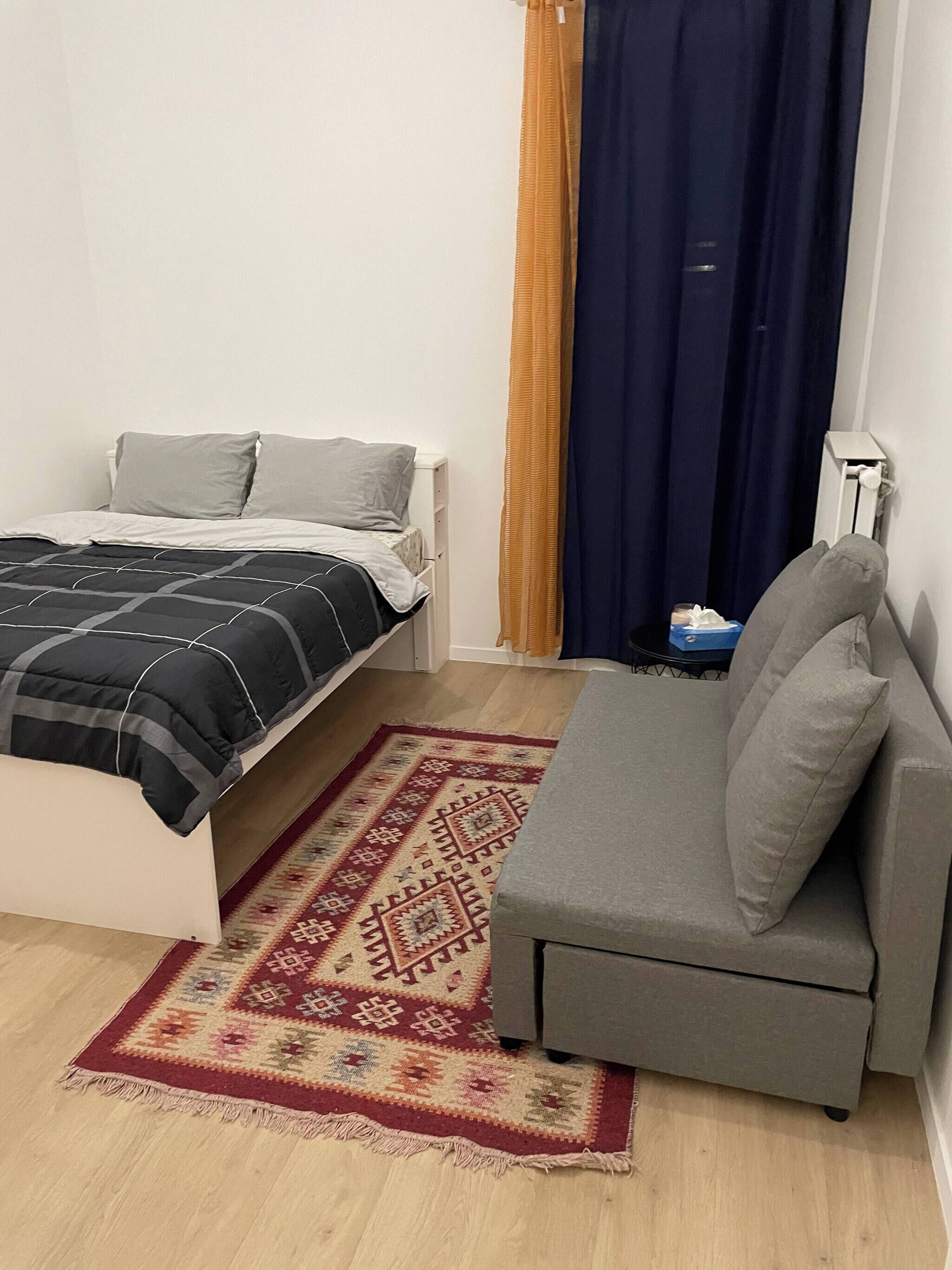 Um quarto com uma cama, um sofá, um tapete estampado e uma cortina.