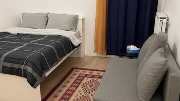 Um quarto com uma cama, um sofá, um tapete estampado e uma cortina.