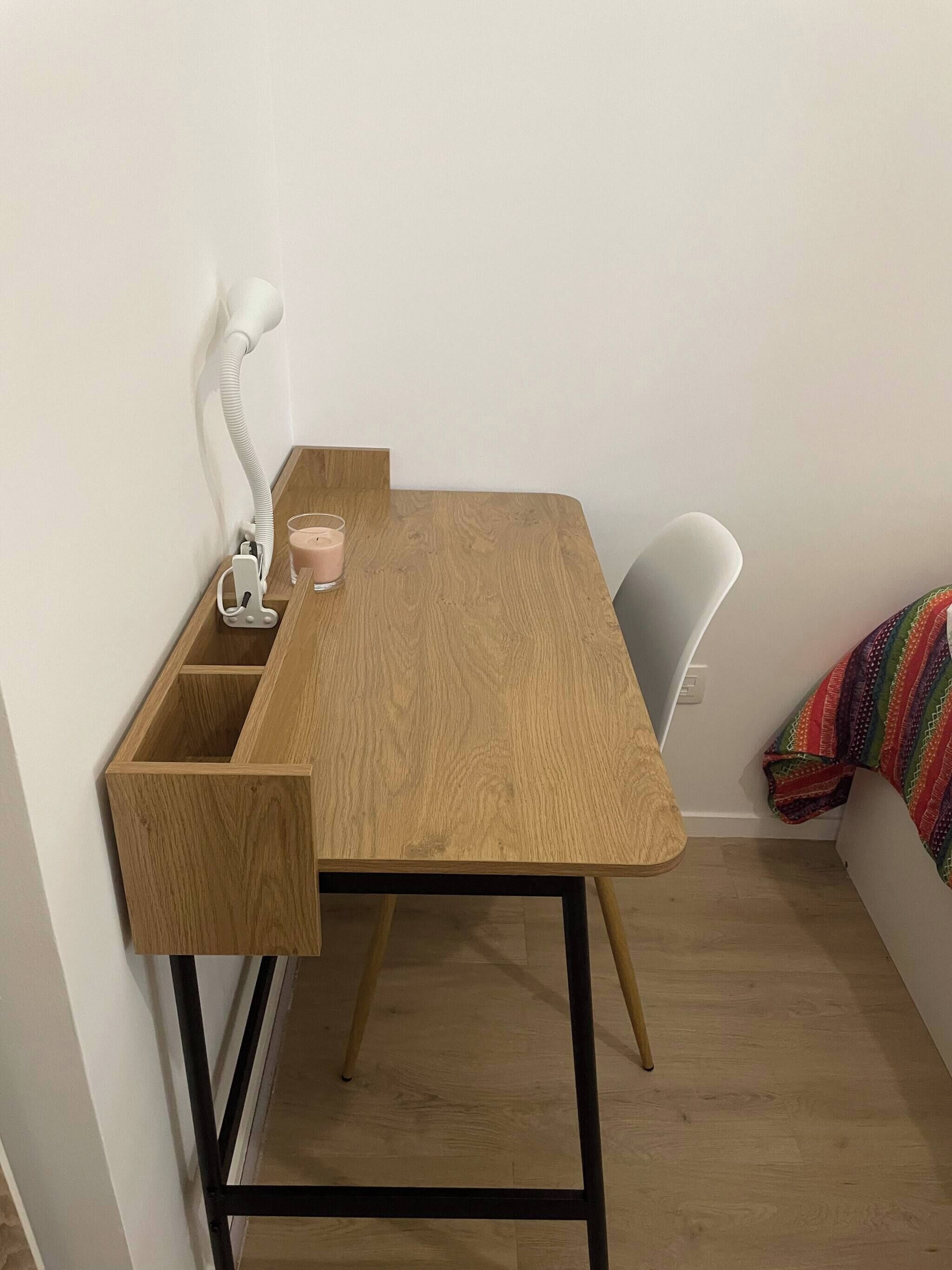 A small wooden desk with a lamp, a glass, and a cup.