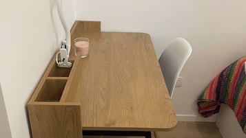A small wooden desk with a lamp, a glass, and a cup.