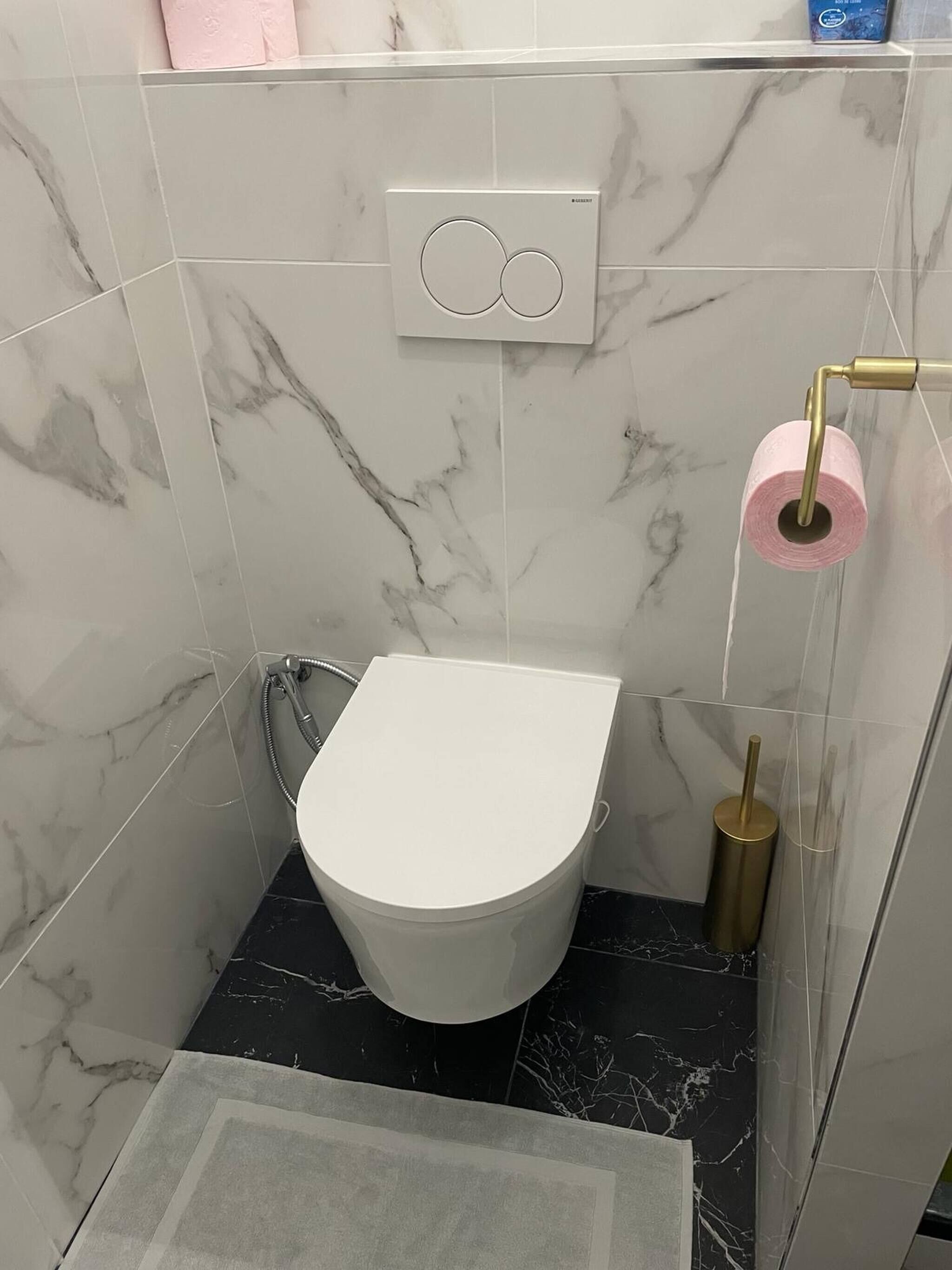 Une salle de bain avec des toilettes blanches, des carreaux de marbre, une douche et un porte-rouleau de papier toilette.