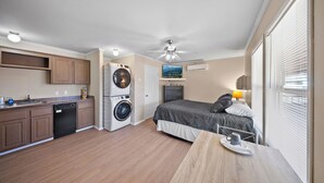 A compact hotel room with a kitchenette, a bed, a dining table, and a washing machine.