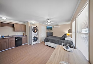 A compact hotel room with a kitchenette, a bed, a dining table, and a washing machine.