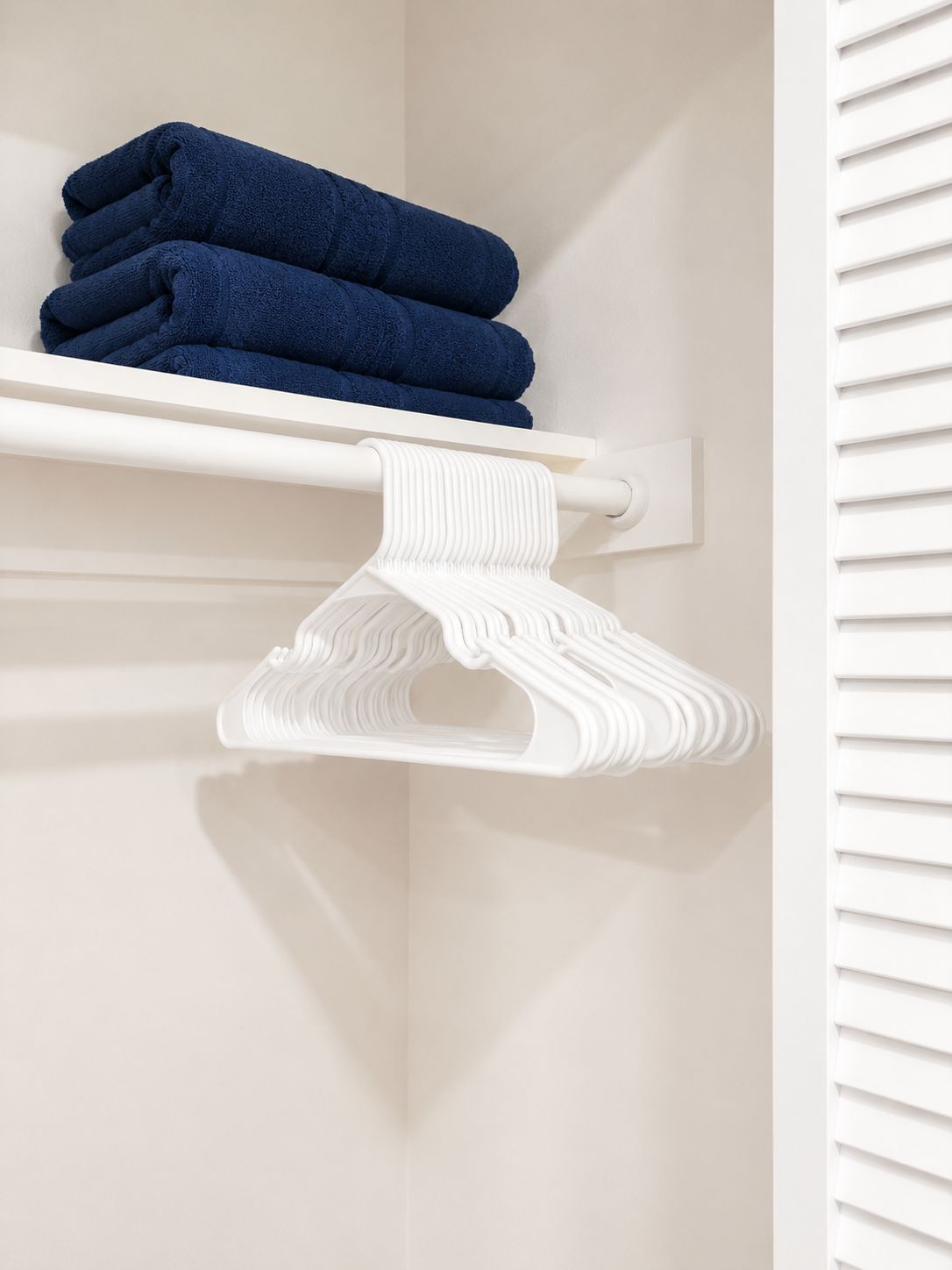 A white towel rack with folded towels and a white garment hanger.
