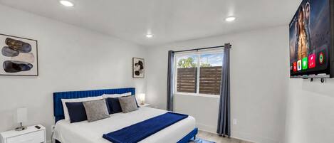 A bedroom with a bed, nightstands, a window with curtains, and artwork on the walls.