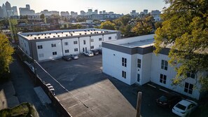 A parking lot with several cars, a building with multiple windows, and a city skyline in the background. - Renovated 2BR - Sleeps 6 - Walk to Deep Ellum/DT (Dallas)
