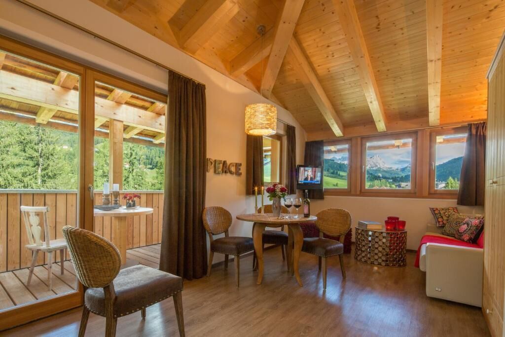 A wooden interior with a dining table, chairs, a sofa, and a television.