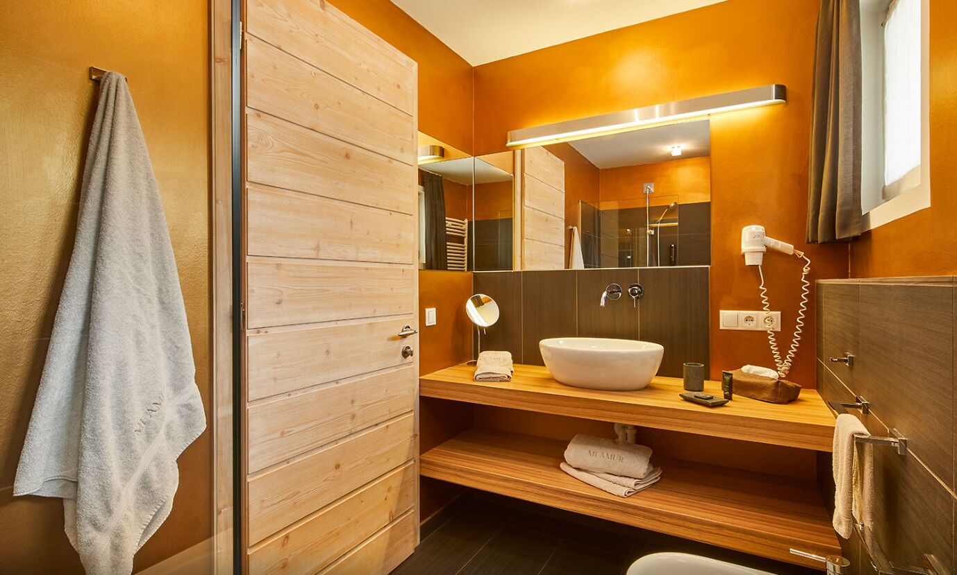 Un baño moderno con tocador de madera, un espejo grande, un lavabo blanco y un perchero para toallas.
