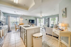 A modern kitchen with a central island, a dining area with a sofa, and a living room with a television. - Gorgeous Ground Floor Condo Just Steps to Pool! (Calabash)