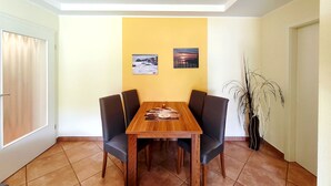 A dining area with a wooden table and four chairs, two wall-mounted pictures, and a potted plant. - Near the beach & newly renovated: Vacation rental at Küstenwaldhaus Koserow - (Koserow)