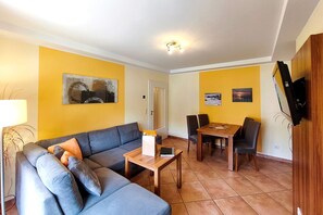 A living room with a sofa, a coffee table, a dining table with chairs, a TV mounted on the wall, and artwork on the walls. - Near the beach & newly renovated: Vacation rental at Küstenwaldhaus Koserow - (Koserow)
