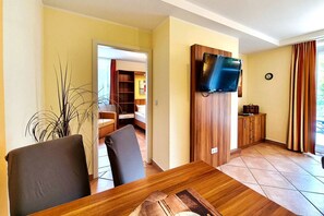 A dining area with a wooden table and chairs, a television mounted on a wooden panel, and a view of a room with a bed and a wardrobe. - Near the beach & newly renovated: Vacation rental at Küstenwaldhaus Koserow - (Koserow)