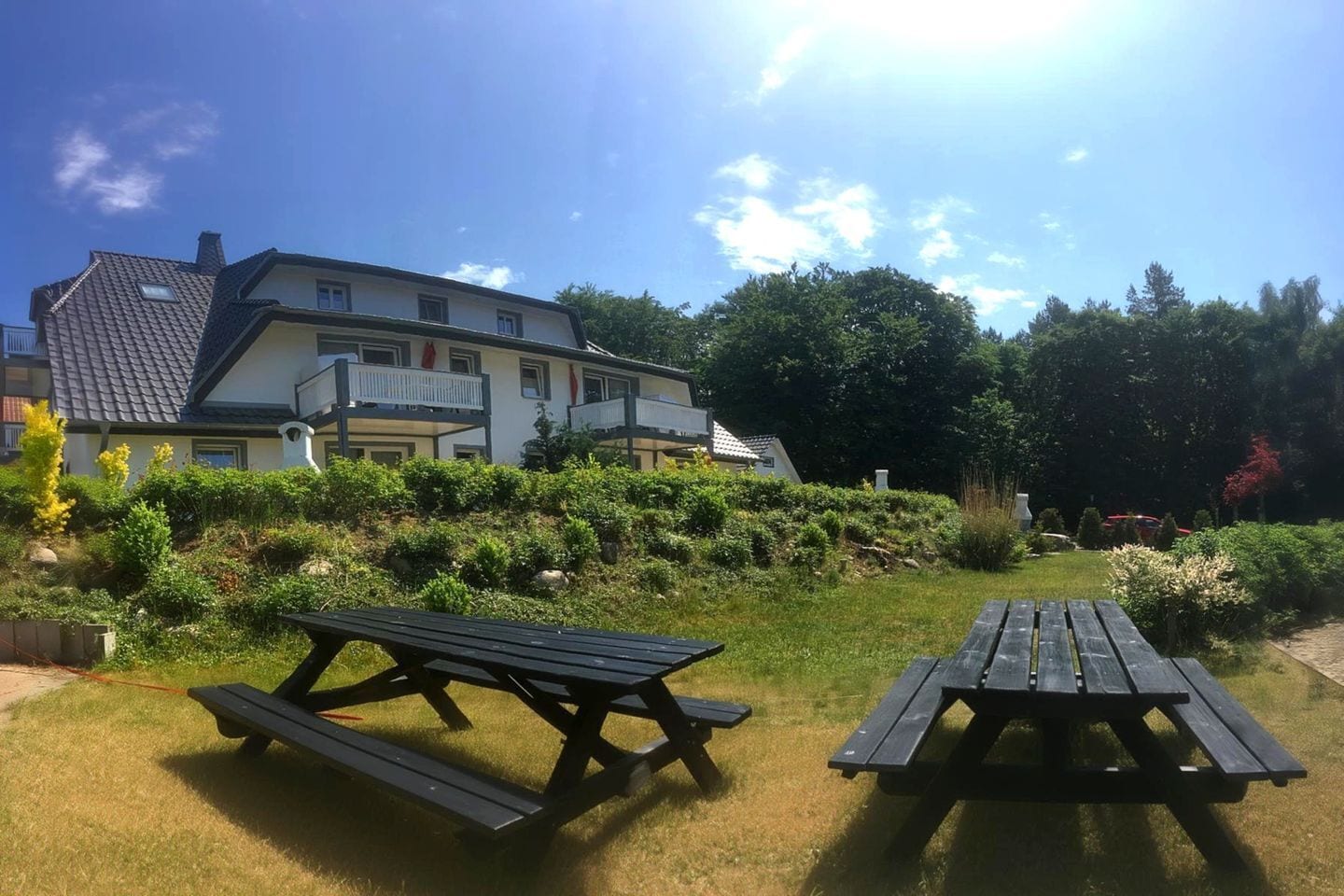 A two-story building with a balcony, surrounded by a well-maintained garden with picnic tables.