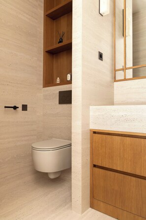 Ein modernes Badezimmer mit Toilette, Holzregalen, einem Spiegel und einer Marmorwand.