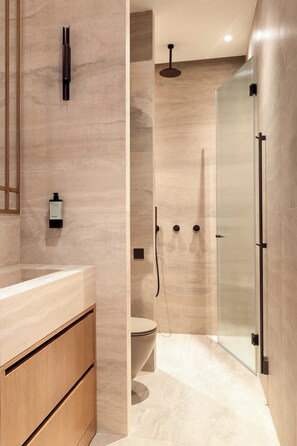 Un baño moderno con piso de mármol, tocador de madera, cabina de ducha de vidrio y un inodoro.