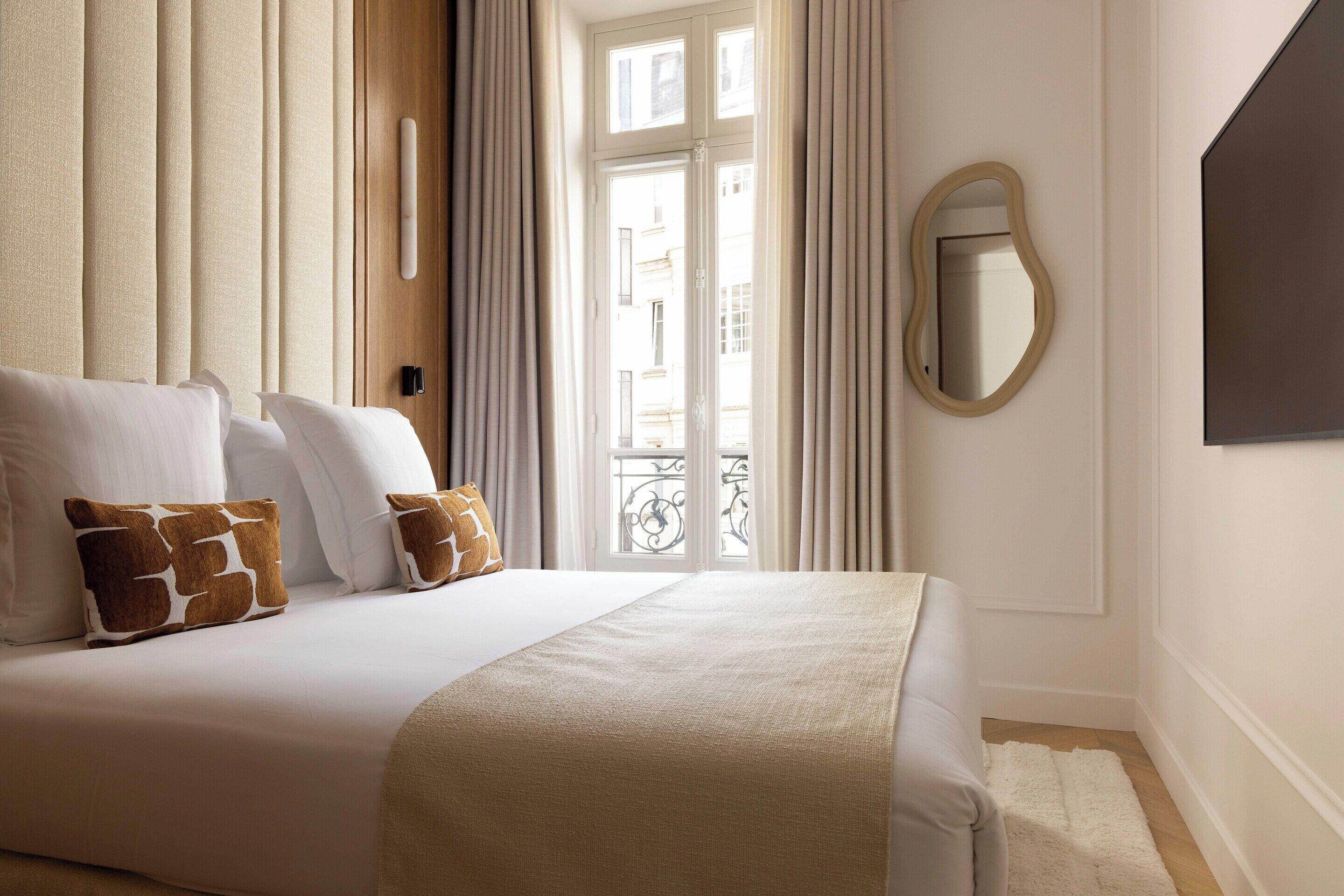 A hotel room with a large bed, two pillows, a mirror, and a view of the outside.