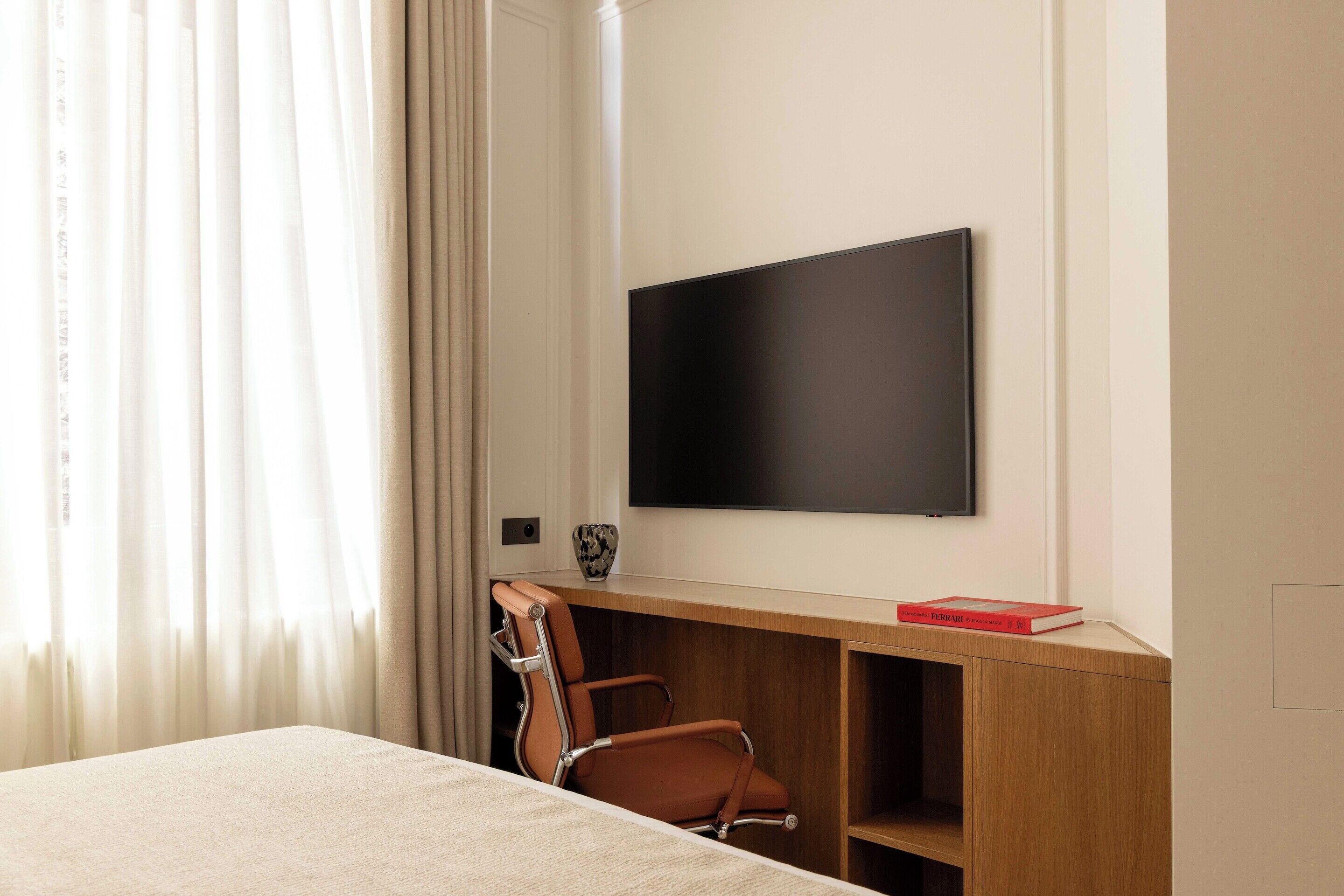 Une chambre d’hôtel comprenant un lit, un bureau avec une chaise, un téléviseur fixé au mur et une fenêtre avec des rideaux.