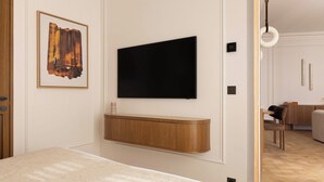 A modern room with a flat-screen TV mounted on a wooden panel, a framed abstract artwork, and a visible dining area with a wooden table and chairs. - Luxury Apt Climatise - 6p/3bdr - Arc de Triomphe (Paris)