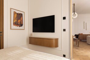 Ein modernes Zimmer mit einem an einer Holzvertäfelung montierten Flachbildfernseher, einem gerahmten abstrakten Kunstwerk und einem sichtbaren Essbereich mit einem Holztisch und Stühlen.