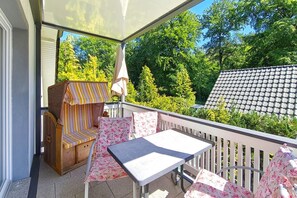 A covered outdoor seating area with a table and chairs, a cushioned bench, and a canopy umbrella. - Pinguin Vacation Rental – Where Nature, a Sauna, and the Sea Await You - Küstenwaldhaus (Koserow)