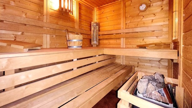 Et sauna rum med træbænke, en trævæg, et ur og en stentønde.